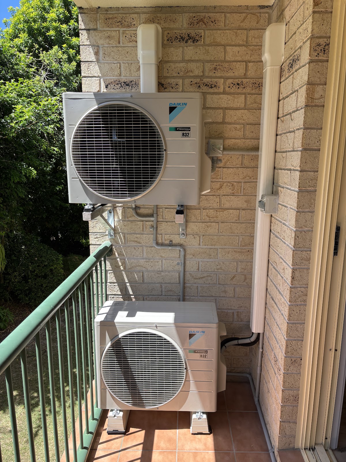 Two Daikin outdoor units mounted one above the other on a balcony wall, with neat white cover ducting