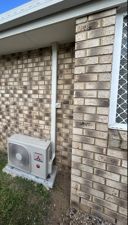 Mitsubishi Electric outdoor unit on a concrete pad beside a brick house